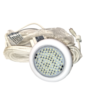 Su di uno sfondo bianco vediamo un faretto LED subacqueo di forma circolare, progettato per l'illuminazione di piscine, specificamente il modello identificato come "Floodlight ghost Piscine Laghetto". Il faretto ha una scocca esterna rotonda realizzata in plastica bianca. La parte frontale è composta da una piastra circolare su cui sono montati numerosi piccoli diodi LED. Questi LED sono disposti in file concentriche e coprono la maggior parte della superficie interna. Si notano anche alcuni componenti elettronici più scuri tra i LED. Dal retro del faretto parte un lungo cavo elettrico di colore bianco, avvolto su se stesso in spire ordinate. All'estremità libera del cavo è presente un connettore elettrico bianco, di tipo stagno, dotato di una ghiera a vite per garantire la tenuta all'acqua una volta collegato. Attaccata al cavo o all'imballaggio c'è un'etichetta adesiva bianca con scritte nere.