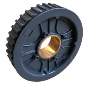 Sullo sfondo bianco si vede un disco piatto e circolare, di colore scuro (nero o grigio scuro). Presenta un ampio foro centrale e dei fori più piccoli disposti sul perimetro interno. La circonferenza esterna presenta una serie di denti regolari (scanalature).Al centro è chiaramente visibile un inserto cilindrico, probabilmente un cuscinetto o una boccola di metallo (colore ottone o bronzo).