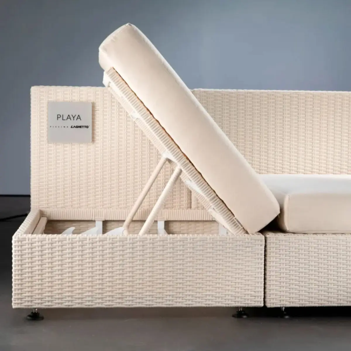 Lettino Living minipiscina Laghetto Playa Un pezzo di arredo living Laghetto in fibra sintetica di colore chiaro, con un design moderno e funzionale. Il divano è composto da due sezioni: una sezione principale con un cuscino di seduta e una sezione laterale con un cuscino di schienale reclinabile. Il divano è realizzato in fibra sintetica intrecciata a mano, con una texture a nido d'ape. Il colore è bianco. I cuscini sono di colore beige chiaro sono realizzati in un tessuto Sky nautico. Il cuscino di seduta è piatto, mentre il cuscino di schienale è reclinabile, sostenuto da un meccanismo metallico a vista. Sulla parte superiore si vede la parete verticale della piscina Laghetto Playa, è presente un'etichetta quadrata con la scritta "PLAYA" e il logo "LAGHETTO".