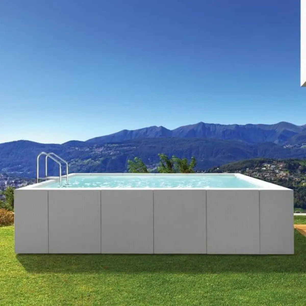 La piscina è di tipo fuori terra, con una struttura rettangolare e rivestita esternamente con pannelli dal design moderno, in fibra sintetica intrecciata a mano di colore bianca. L'acqua all'interno è cristallina e riflette la luce del sole, creando un effetto rinfrescante.