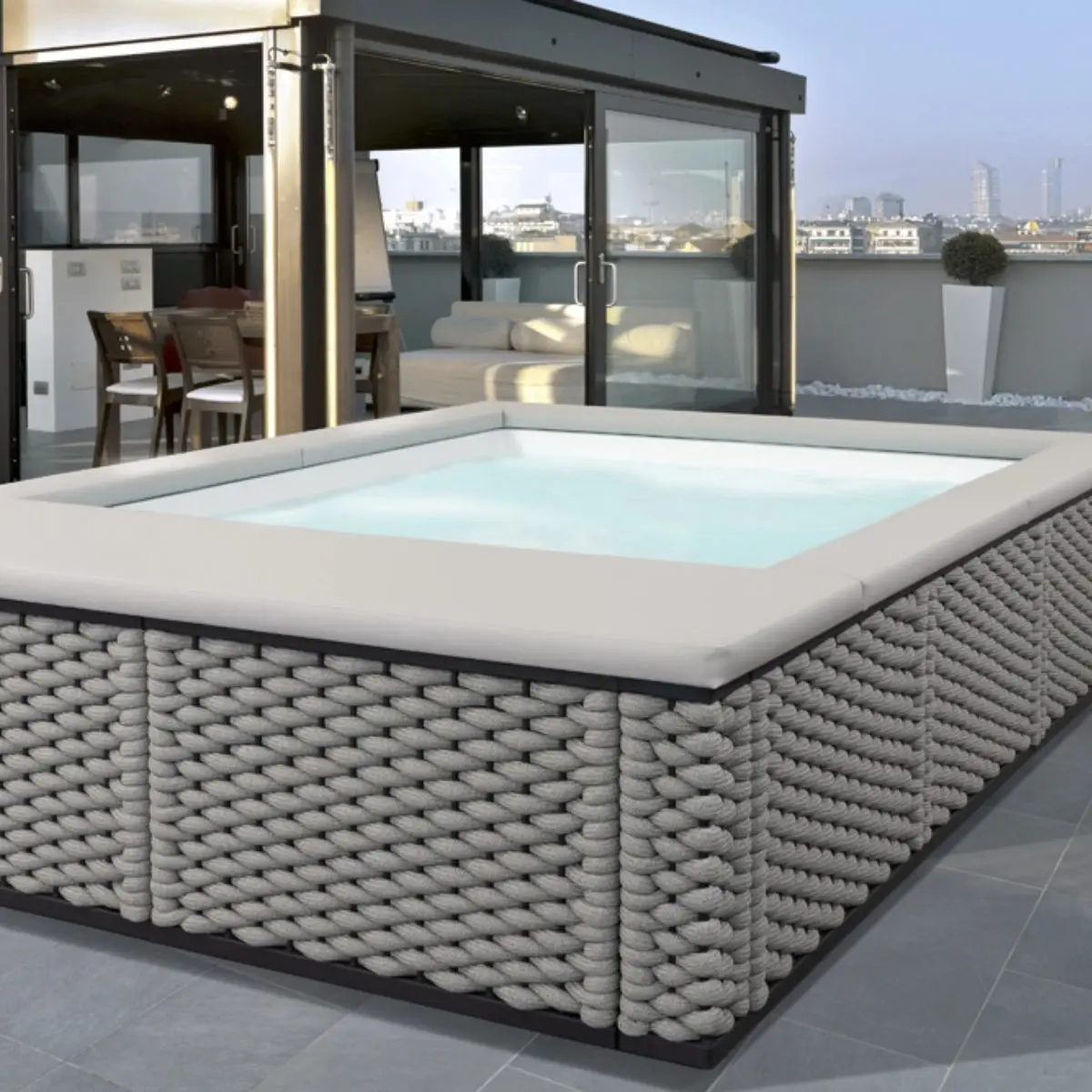 Piscina fuori terra Laghetto Ninfea con rivestimento in corda. Presentata in un terrazzo outdoor. Colore rivestimento Stone, colore cuscino grigio chiaro.