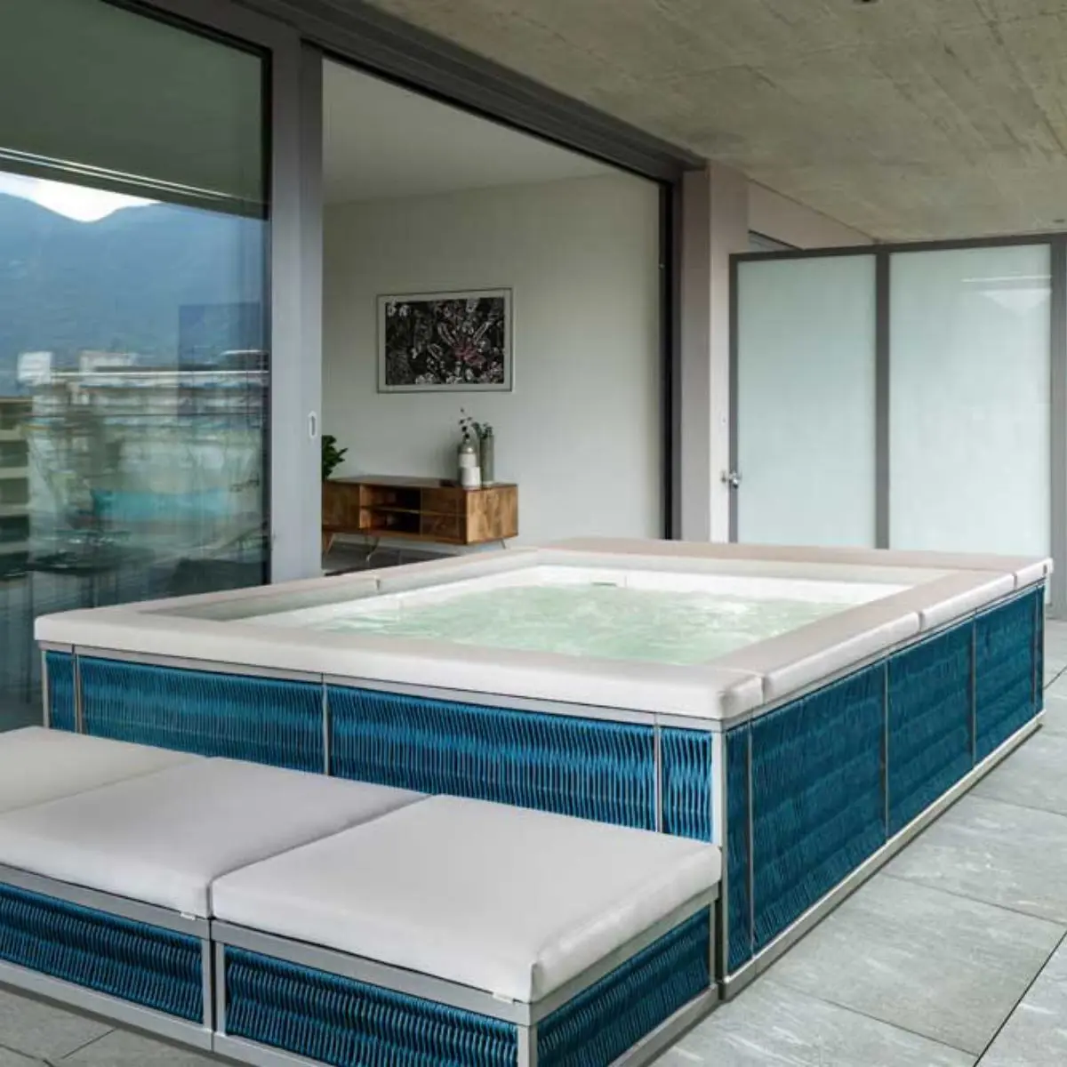 Piscina fuori terra Laghetto Ninfea Thiny con rivestimento in corda. Presentata in un terrazzo outdoor. Colore rivestimento Deep Blue, colore cuscino bianco.