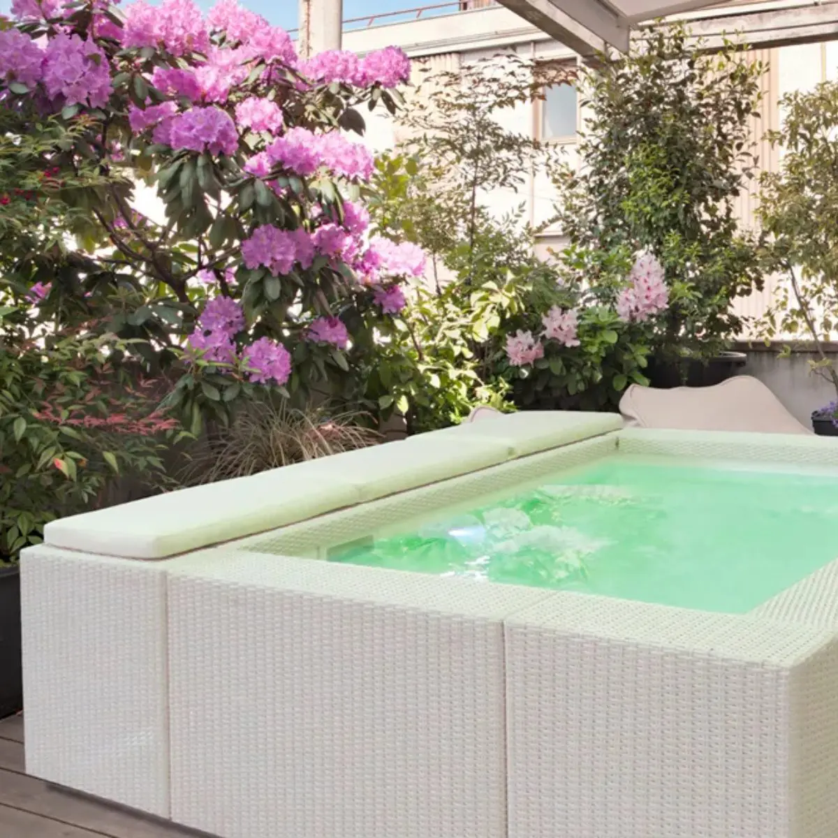 Piscina fuori terra Laghetto Playa con rivestimento in fibra sintetica intrecciata effetto rattan. Presentata in un contesto outdoor. Colore rivestimento bianco, colore cuscino bianco.